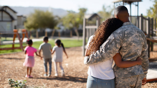 A couple watches their young children run on a playground holding hands.