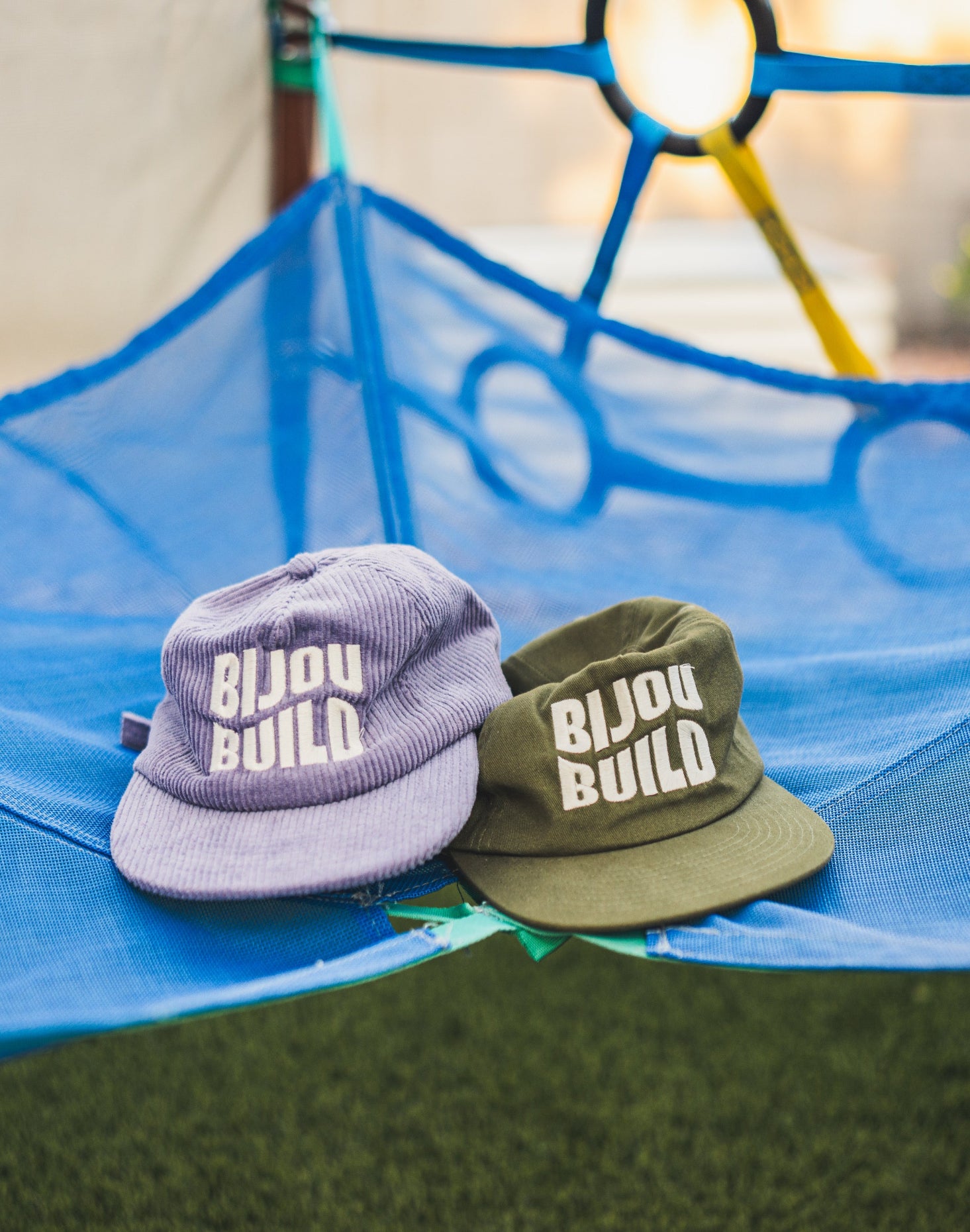 Two hats with 'Bijou Build' logo on a blue hammock