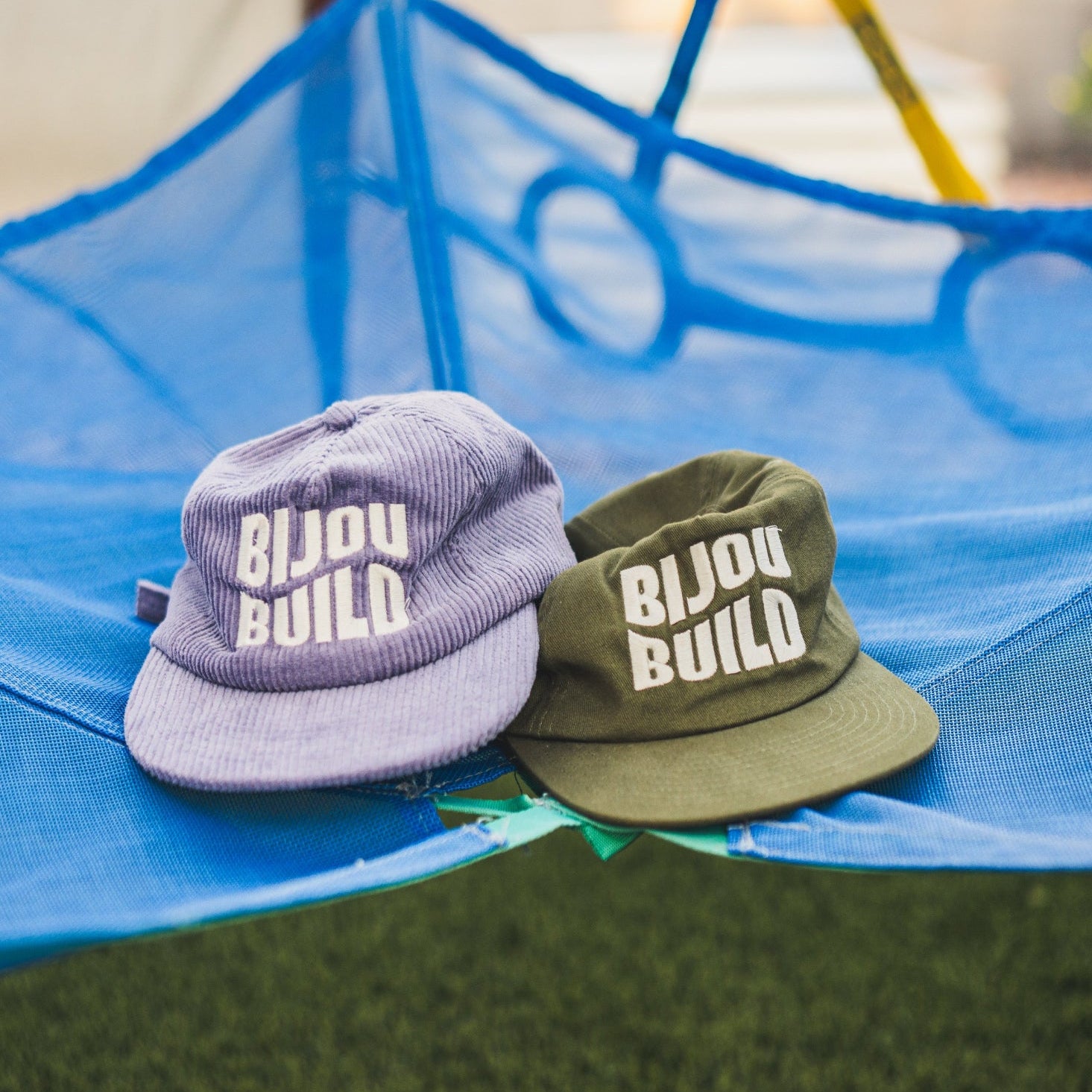 Two hats with 'Bijou Build' logo on a blue hammock