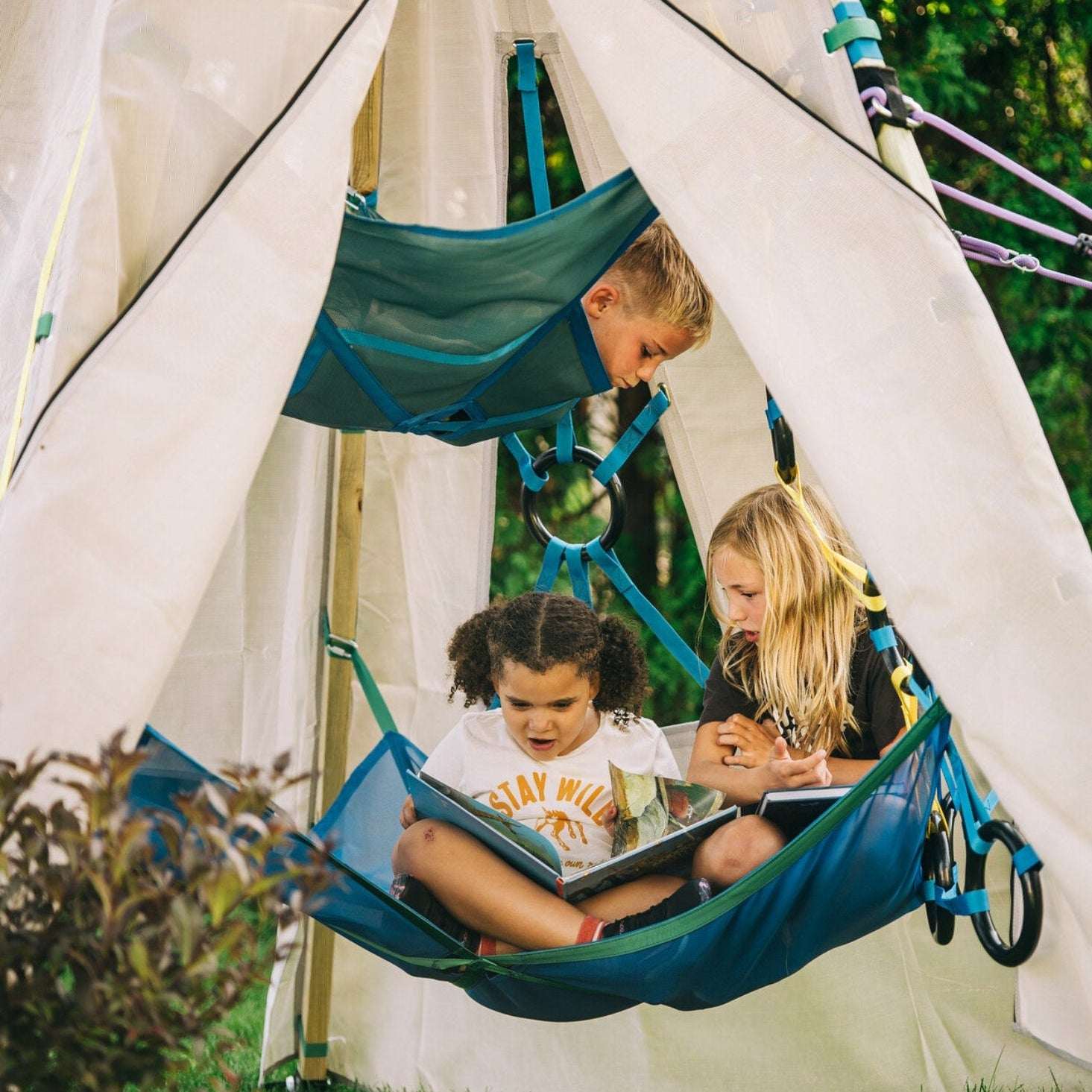 Children reading books in blue hammocks attached to a white teepee.
