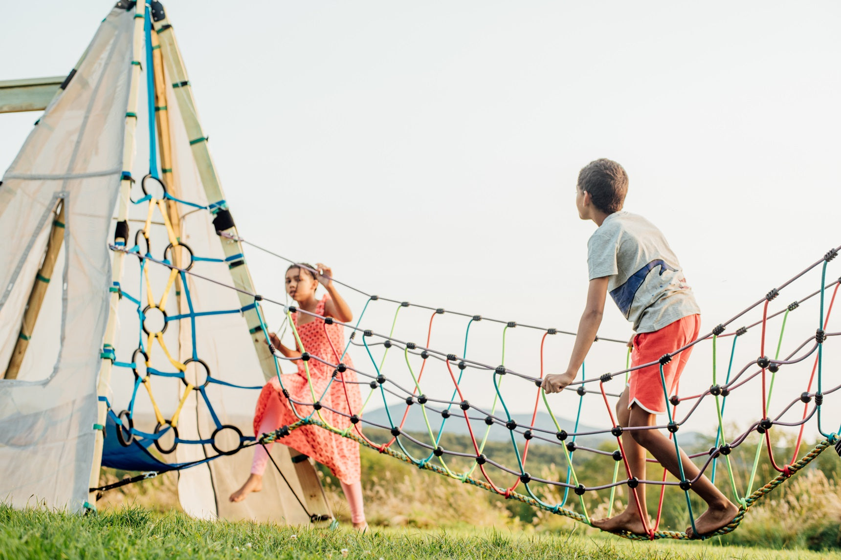 Two children play on a colorful rope climbing structure outdoors.