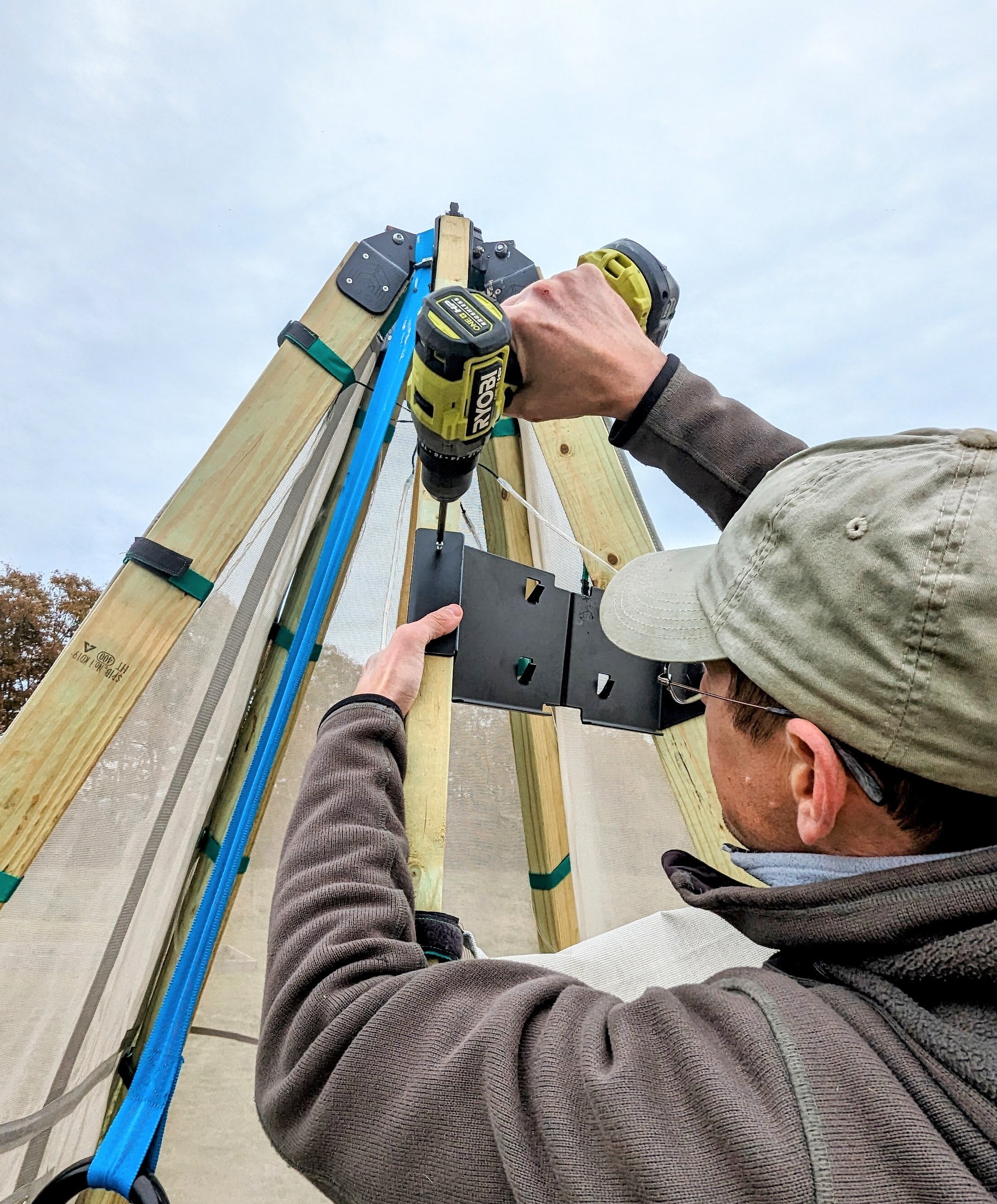 Person using a drill to assemble a wooden structure outdoors.