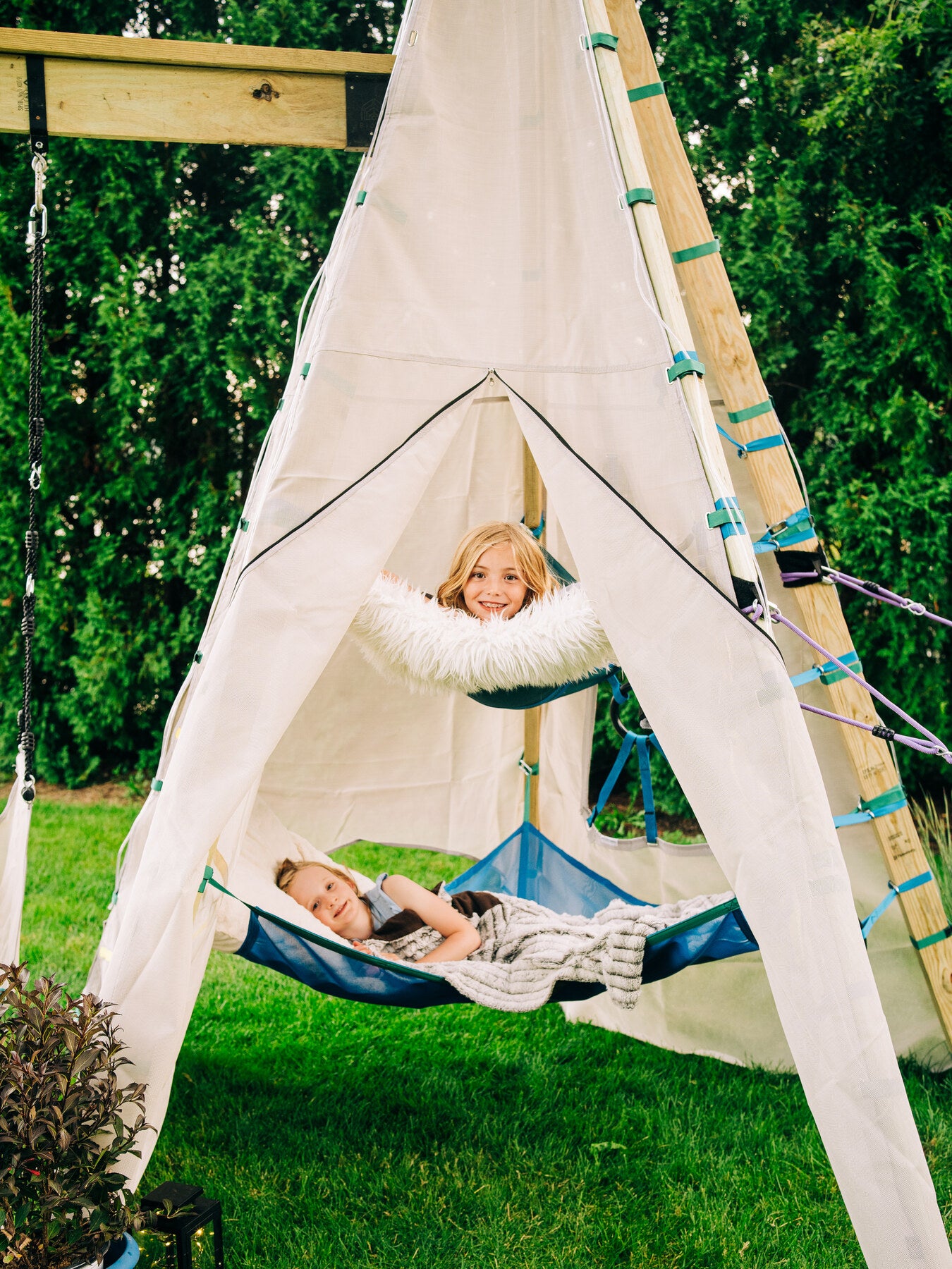 Children relaxing in a play tent with hammocks on a grassy area.