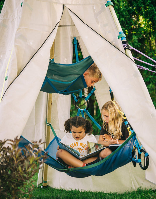 Children reading books in blue hammocks attached to a white teepee.