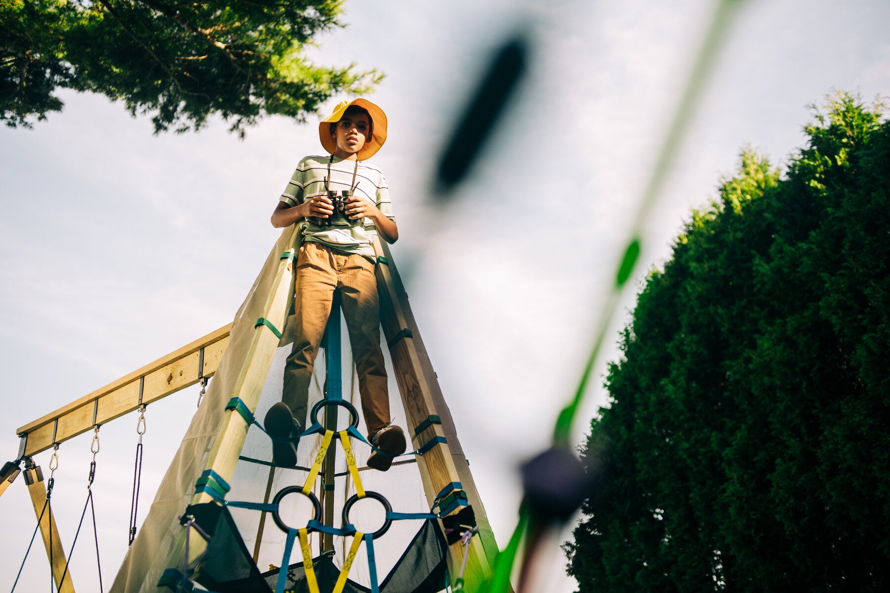 Child on a playground structure wearing a hat and holding binoculars.