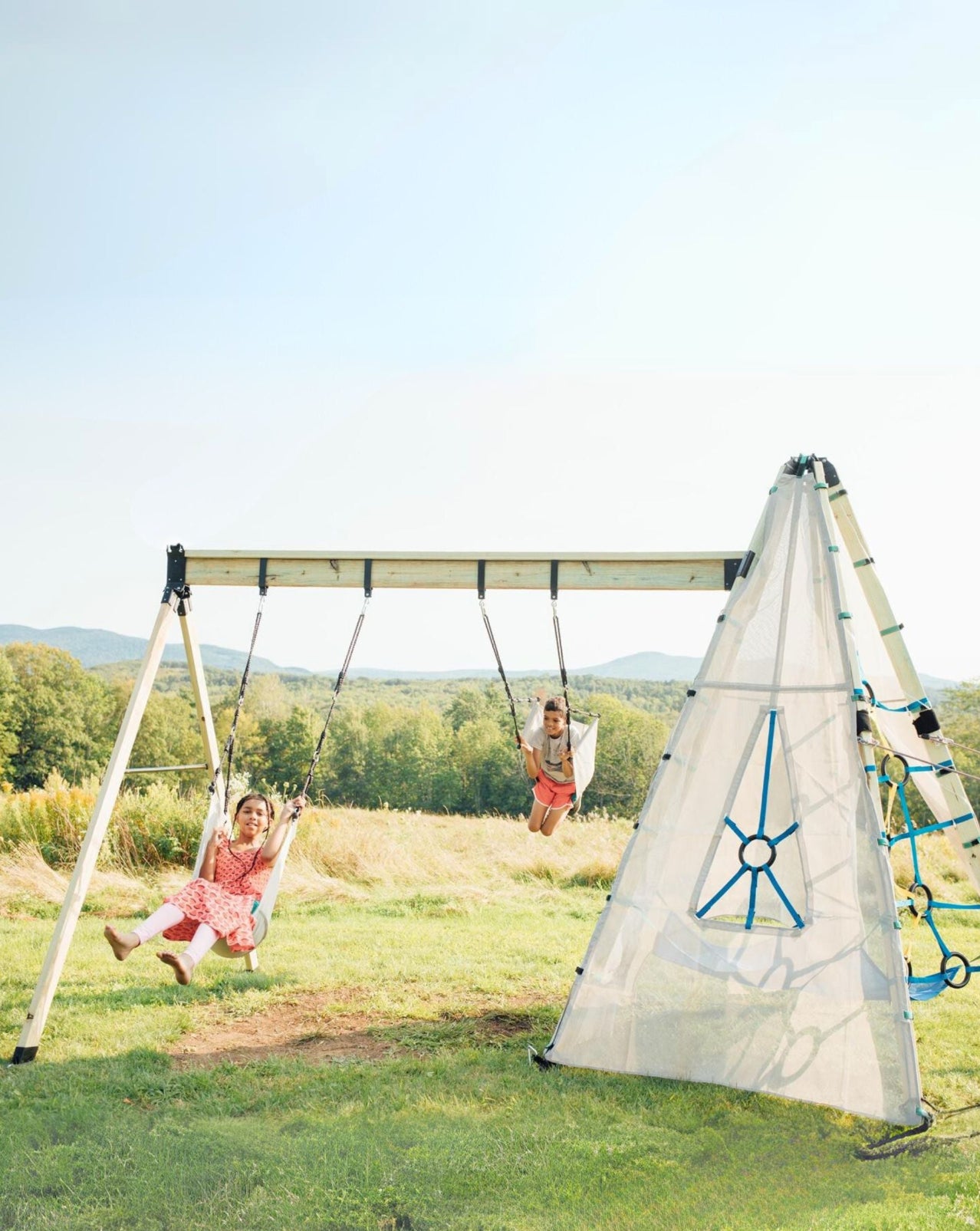 Children swinging on a playground set in a grassy field on a sunny day.