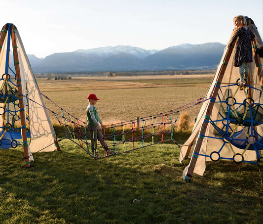 Children playing on a rope climbing frame set up outdoors with mountains in the background