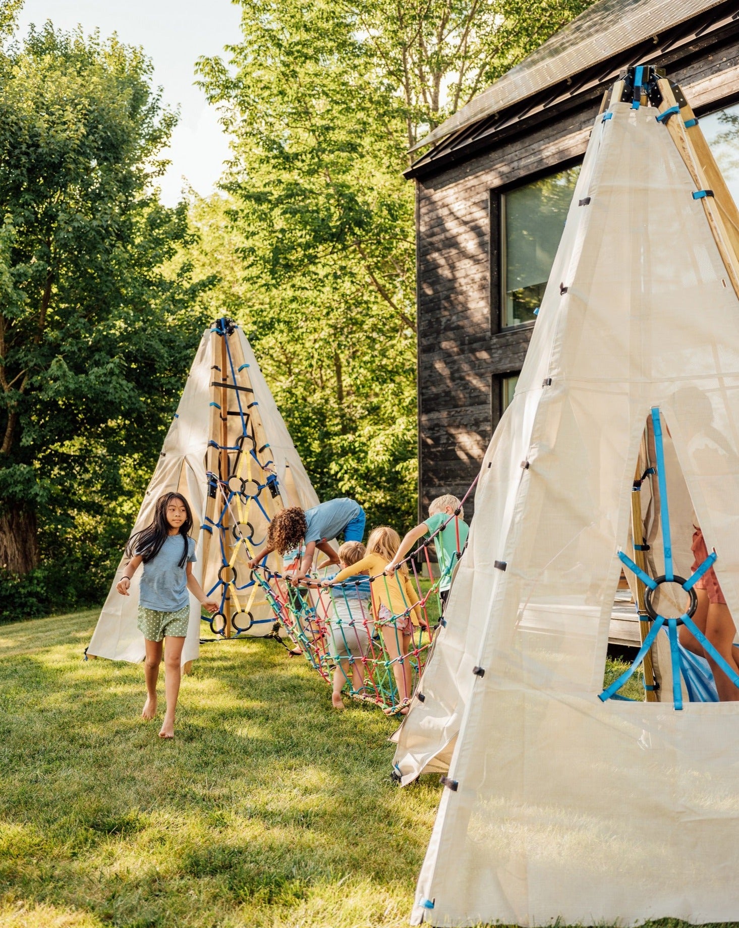 Children playing on outdoor climbing structures near a house on a grassy yard.